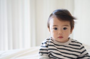 Asian baby wearing a striped shirt, sitting alome, looking at the camera.